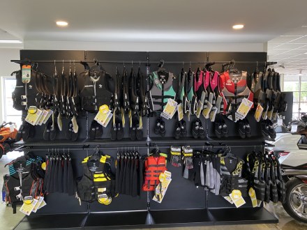 Life vests and protective vests hanging on a black rack in the middle of a store.