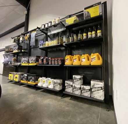 Various motor oils and other fluids used for powersports sitting on shelves against a wall.